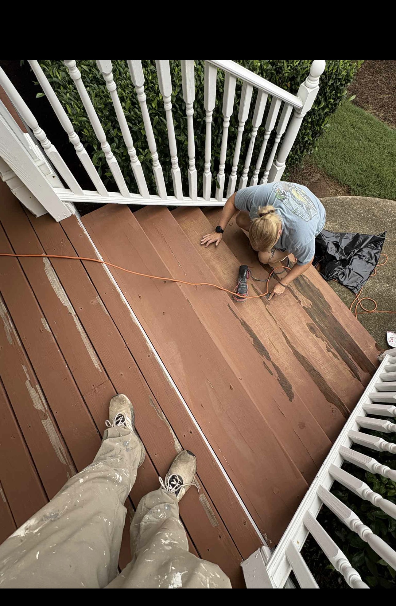 Deck restain in progress — worker applying fresh stain to weathered boards