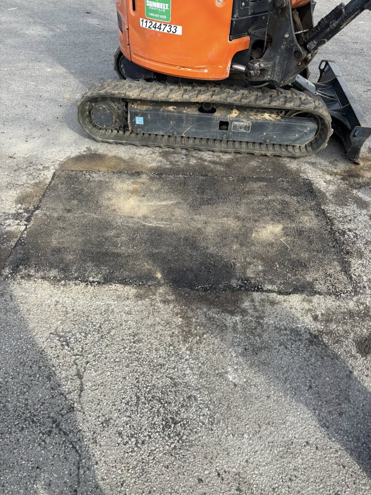 Mini excavator finishing a fresh asphalt patch in a driveway