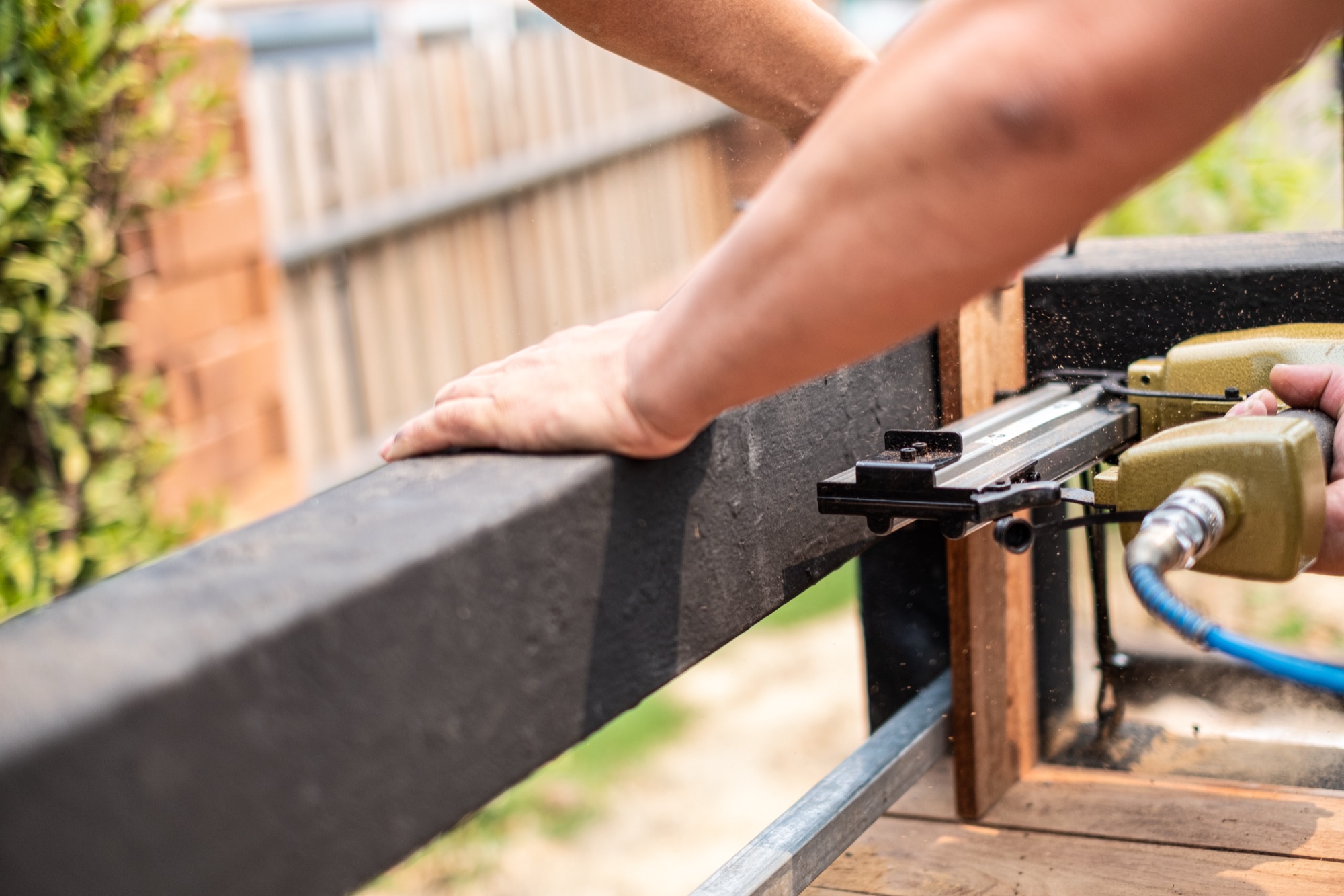 Contractor nailing pressure-treated lumber into place during a fence installation