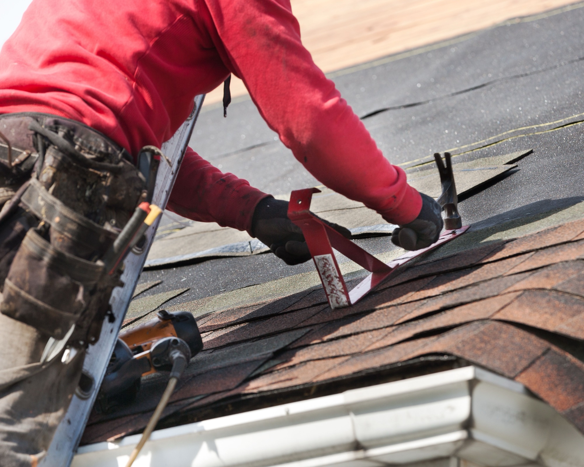 Roofer hammering an asphalt shingle into place during a roof repair